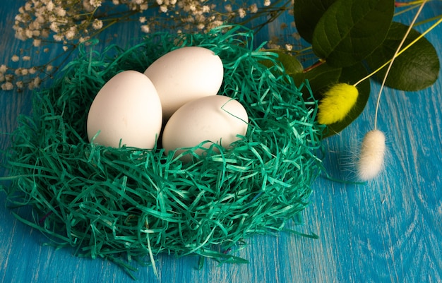 Small green nest with white eco eggs with flowers on light-blue wooden