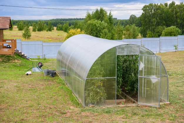 a small greenhouse with plantings inside is near the house next to it grows green plants and grass