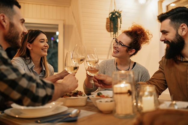 Small group of happy friends having fun while toasting during dinner at home Focus is on redhead woman