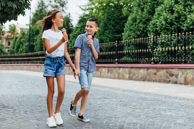 Small and happy friends walking in the city and eating sweet ice cream together.