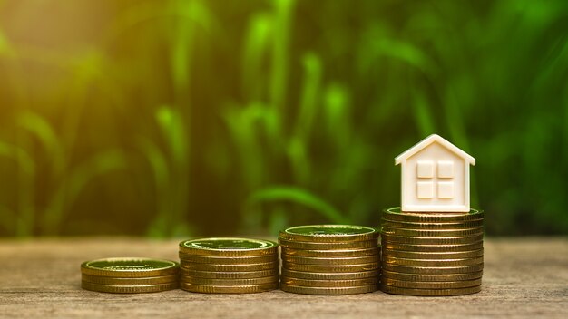 Small house on stack of golden coins in the garden. - Concept of Investment property.