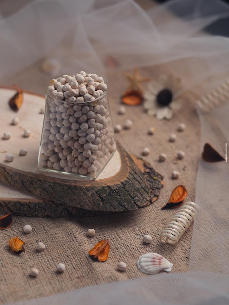 A small jar of balls sits on a piece of wood with a white and brown decoration on it.