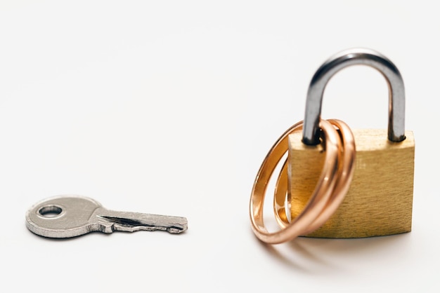 Small key and two golden wedding rings locked on a padlock