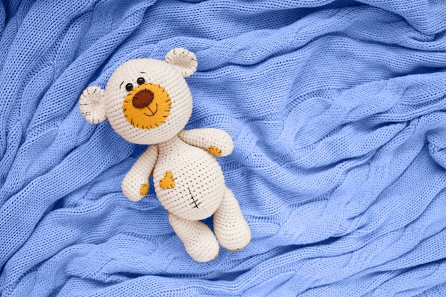 A small knitted amigurumi baby toy-bear is on a blue blanket