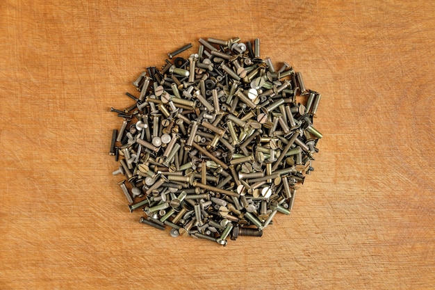 Small metal bolts and screws of different sizes and colors are scattered on a wooden table in the center with a small pile