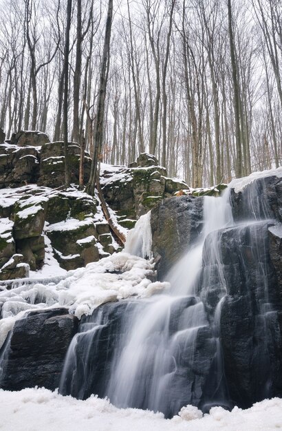 A small mountain waterfall is covered in snow. Stream in the forest, winter landscape, light background