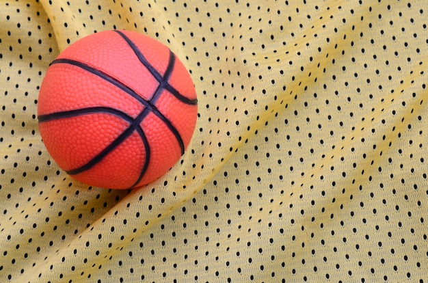 Small orange rubber basketball lies on a yellow sport jersey