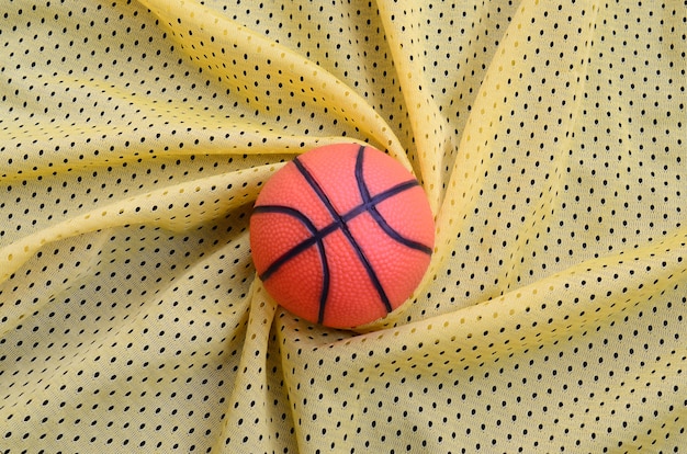 Small orange rubber basketball lies on a yellow sport jersey 