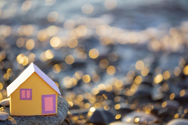 A small paper house against the backdrop of the sea at sunset the concept of real estate services a