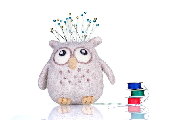 Small pillow for needles in the form of an owl with threads on a white background