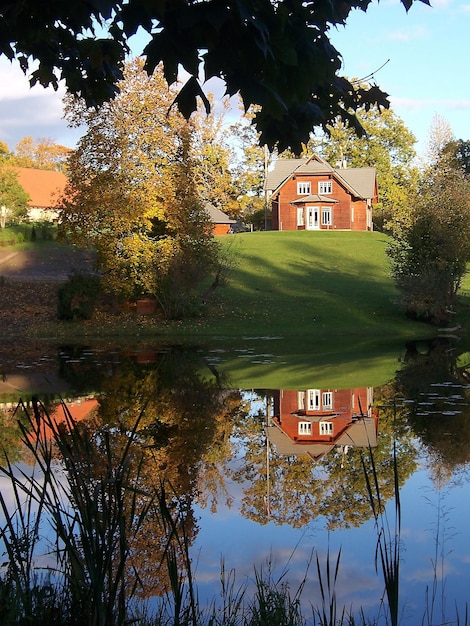 A small red house on a green hill is reflected in the mirror surface of the pond