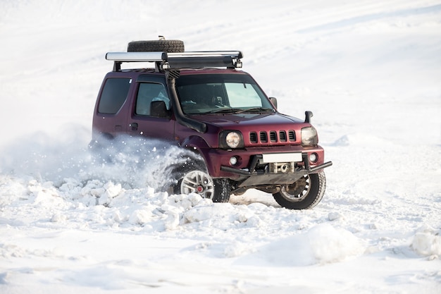 Small red japanese SUV riding on snow and snowflakes flying from its wheels