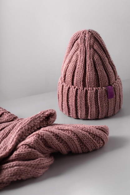 Small red knitted hat with on a white scarf jn grey background. woolly hat Closeup. Copy space