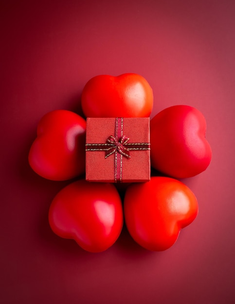 A small red present gift box with ribbon on five heart balls on red background vertical style An essential gift on special days with love birthdays New Years Valentine's Day and anniversaries