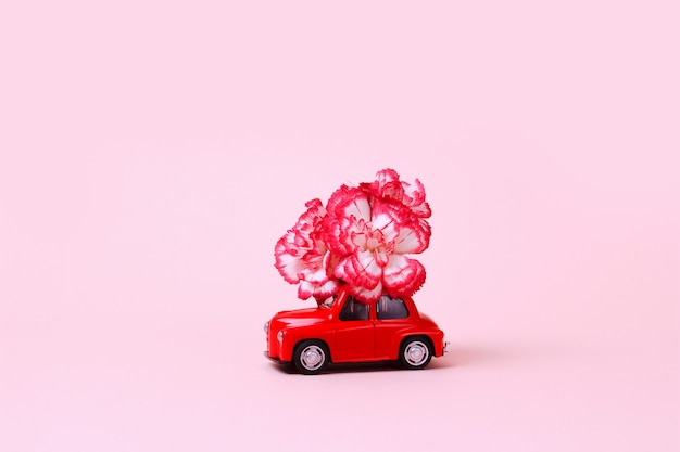 Small red retro toy car with  flower on the roof Delivery of gifts for Valentines Day World Womens Day