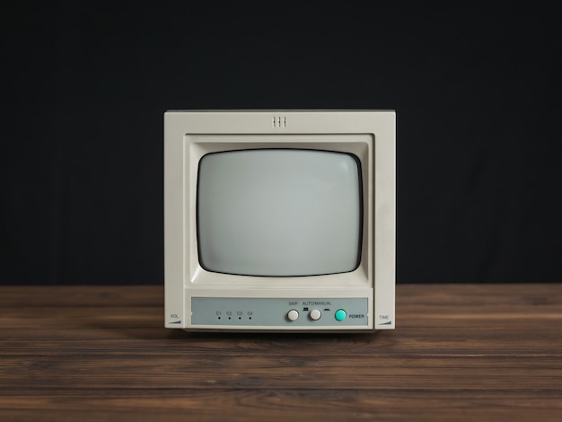 Small retro monitor on a wooden table on a black background. Old video surveillance equipment.