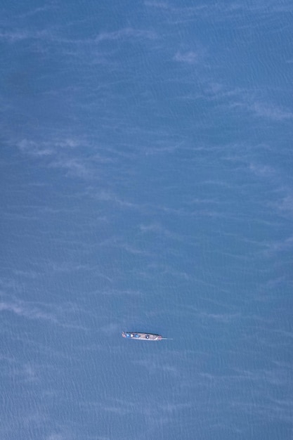 Small riding boat in the middle of the big blue lake with smoggy surface.