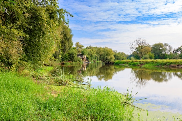 Small river on a background of green trees on the shores against blue sky. River landscape at sunny autumn morning