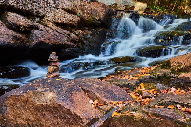 Small rock stack cairn on leafcovered rocks along cascading river waterfalls