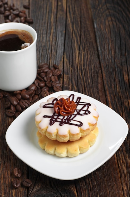 Small round cake with chocolate cream and cup of coffee on dark wooden table