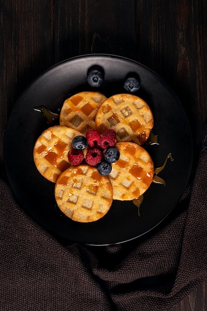 Small round waffles served with blueberries, raspberries and caramel sauce or honey. Copy space.