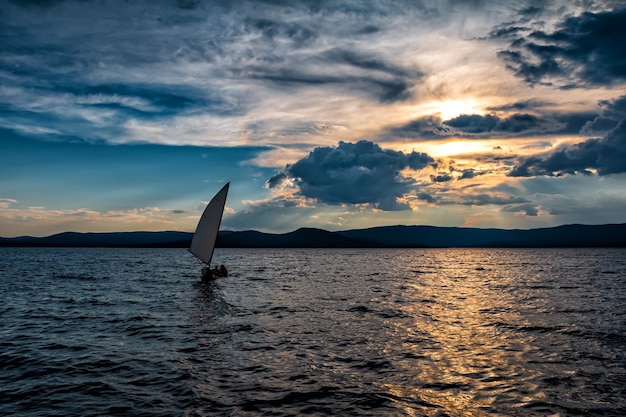 A small sailboat on a picturesque lake on a cloudy evening before sunset