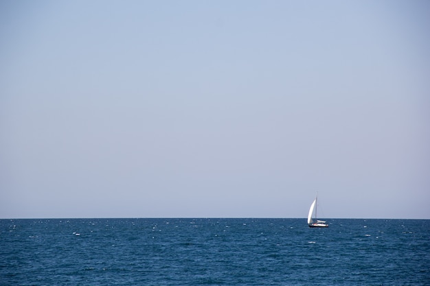 Small sailing yacht with big white sails in the open sea on the horizon in summer