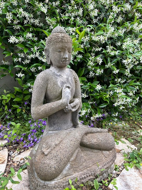 Small sculpture of Buddha in the garden with blooming jasmine