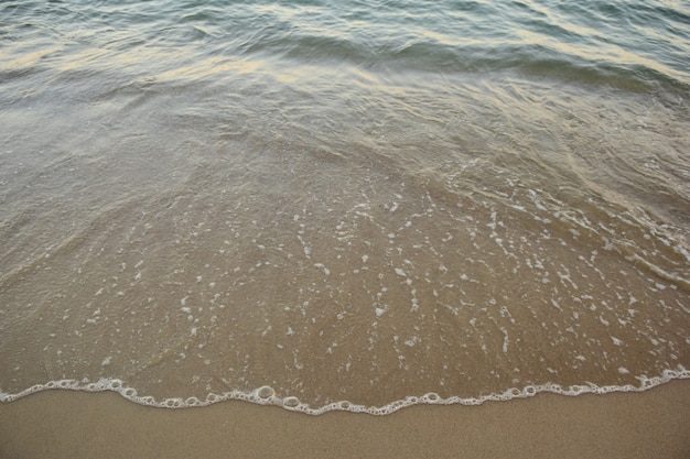 A small sea wave rolls over the sandy beach with transparent water with a foamy edge. Photographed from the top