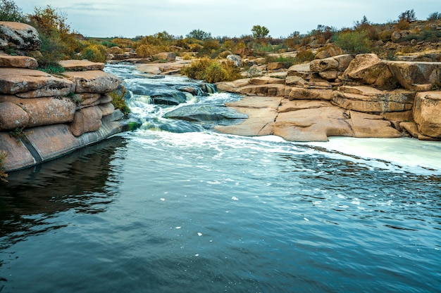 A small shining stream flows among smooth wet and dark stones and dry low trees