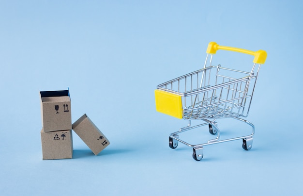 A small shopping trolley and boxes on a blue surface. Shopping concept, side view.