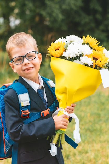 Small smiling boy with flowers ready to go in first class in school schoolboy in a school uniform