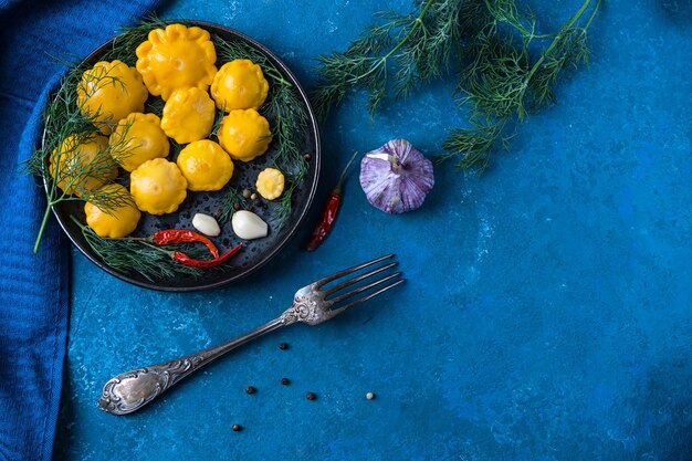 Small squash marinated with pepper, garlic and dill, homemade. On the blue table. View from above. Copy space. Fermented food.