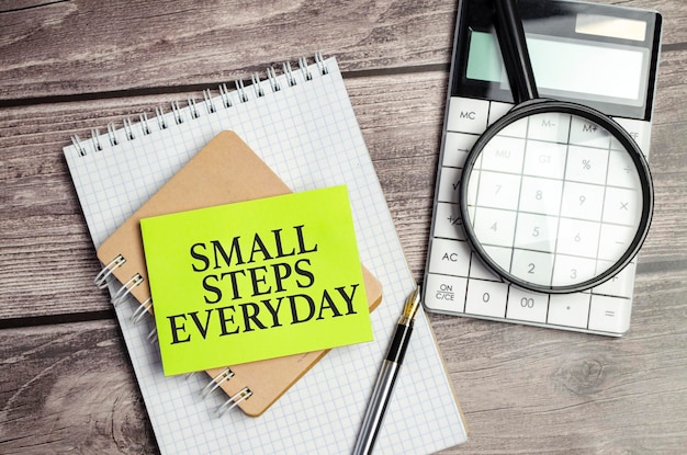 Small steps everyday words on green sticker and calculator magnifying glass on wooden background