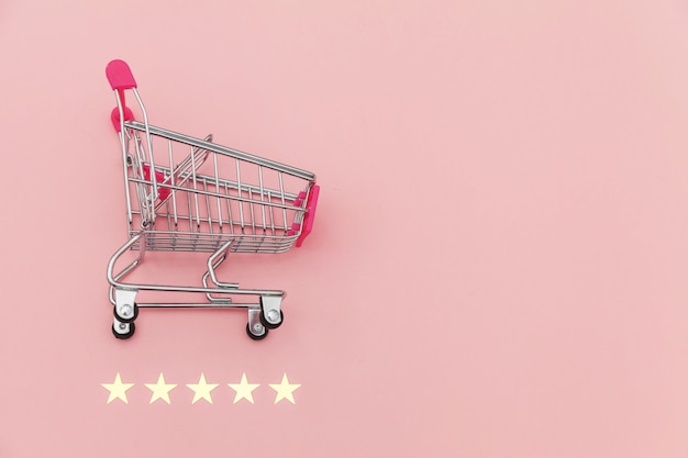 Small supermarket grocery push cart for shopping toy with wheels and 5 stars rating isolated on pastel pink background. Retail consumer buying online assessment and review concept.