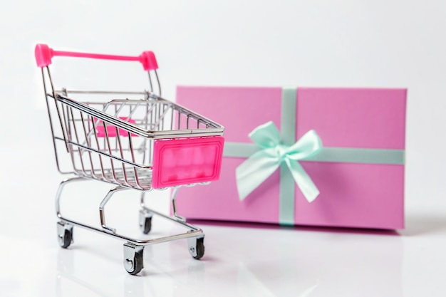 Small supermarket grocery toy push cart and gift box on white background