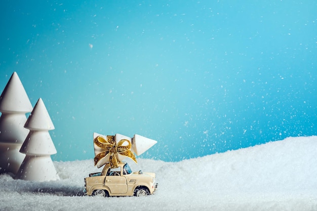 A small toy car transporting Christmas tree in the middle of snowy forest