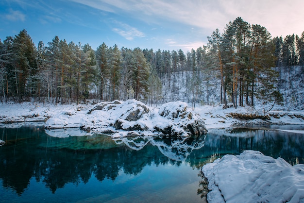 small turquoise lake in the mountains among snow-covered forest.