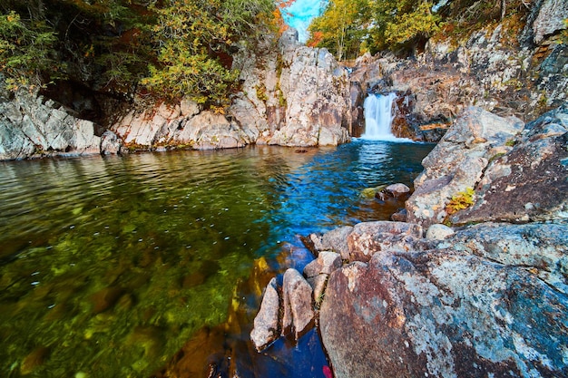 Small waterfall over rocks into blue and green river next to huge boulders in forest