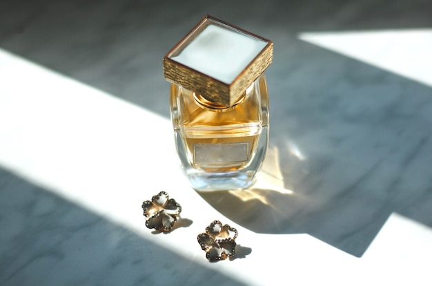 Small wedding flower earrings and stylish perfume scent bottle on the grey background in sun lights.