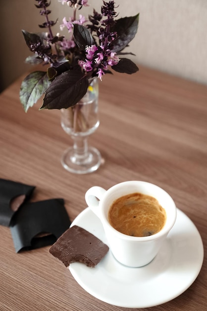 Small white cup of espresso coffee with bitten piece of chocolate on saucer