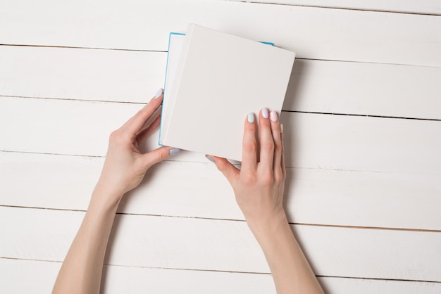 Small white half-open box in female hands. Top view. White table on the 