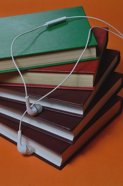 Photo small white, wired headphones lie on top of a stack of books. close-up