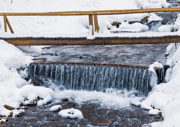 Small wooden bridge over a cold mountain stream in a winter forest valley in the beautiful Carpathian mountains