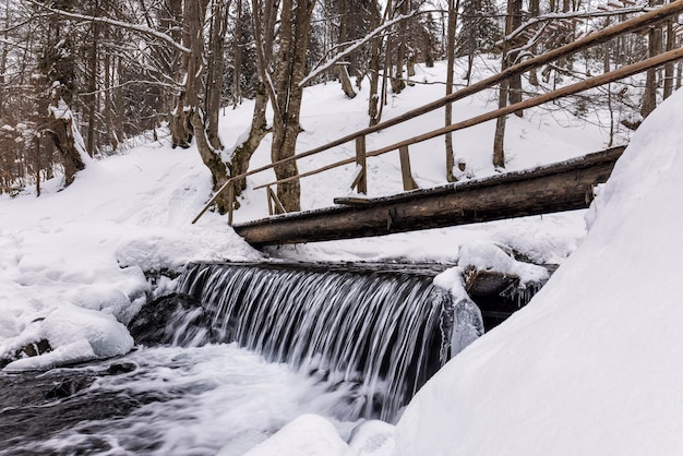 Small wooden bridge over a cold mountain stream in a winter forest valley in the beautiful Carpathian mountains