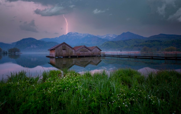 a small wooden house sits in the grass near a lake