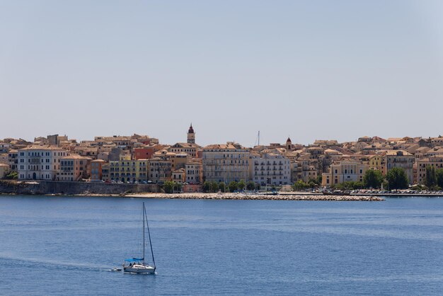 Small yacht with assembled sails against the backdrop of embankment of Corfu, Ionian islands, Greece