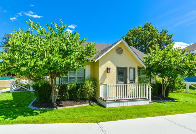 Photo small yellow family house on sunny day with green lawn and concrete pathway