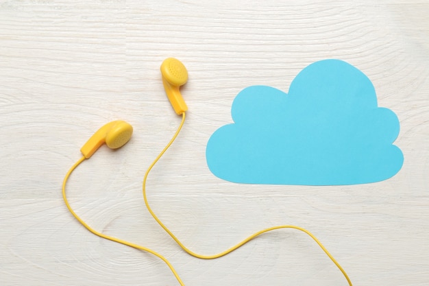 Small yellow headphones and a blue cloud of paper on a white wooden background. top view