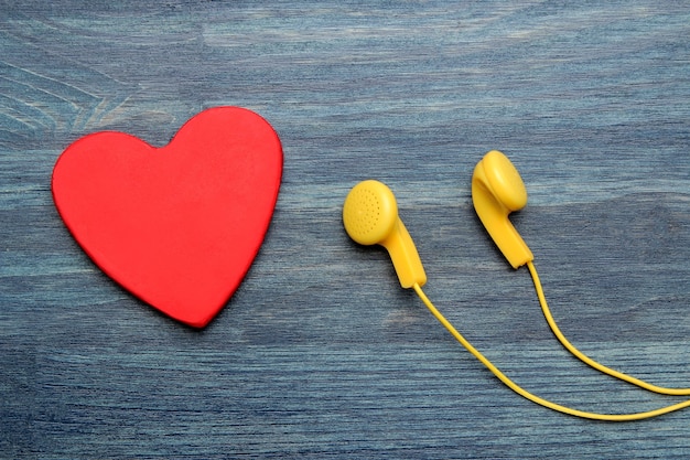 Small yellow headphones and red decorative heart on a blue wooden background. top view